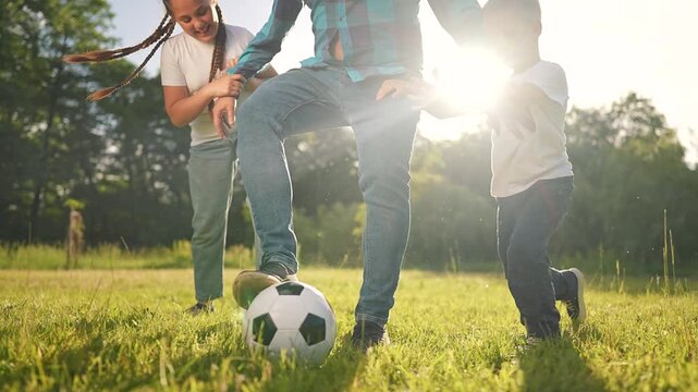 On the field, the boy, the girl, and the man their father are playing a game of soccer. The children compete for the football with laughter and joy. It a perfect day of playing and being children.