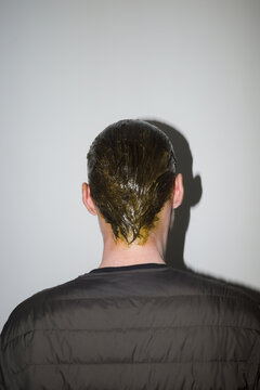 Person with wet dyed hair stands against a plain wall