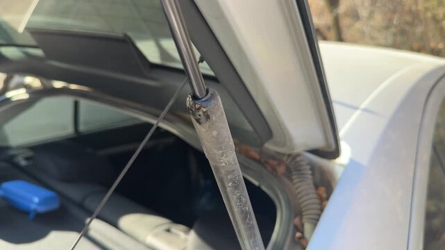 Gas strut extends and compresses as the car trunk lid opens and closes, hatch support mechanism, cargo access, automotive maintenance, vehicle operation.