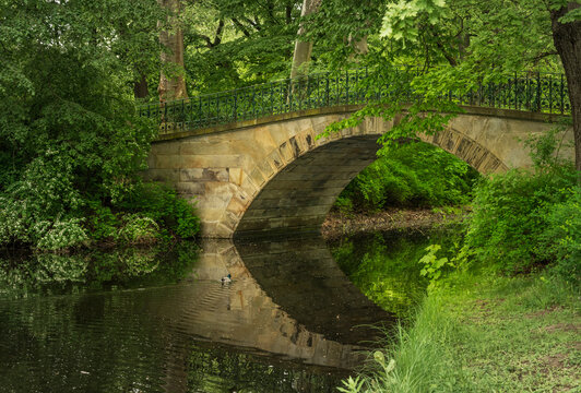 The Augustenbrucke, a historic stone arch bridge with an ornate railing, spans a tranquil waterway in Georgengarten, Hanover, Lower Saxony.
