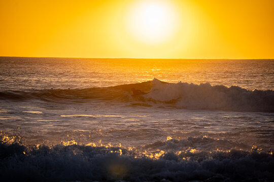 View of a surfer riding a breaking wave during a vibrant golden sunset over the Atlantic Ocean in El Cotillo, Canarias, Spain.