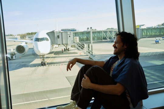 Man relaxing by airport window watching airplane