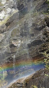Vertical waterfall with moving rainbow in sunlight, water spray and mist creating colorful natural scenic landscape, no people. Peaceful nature scene