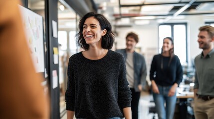 Fototapeta premium A group of young professionals casually interacting in a modern office space, with a woman in the foreground smiling and engaging with colleagues.