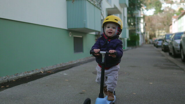 Toddler riding scooter on residential street wearing helmet exploring neighborhood with confidence independence balance childhood adventure urban family lifestyle
