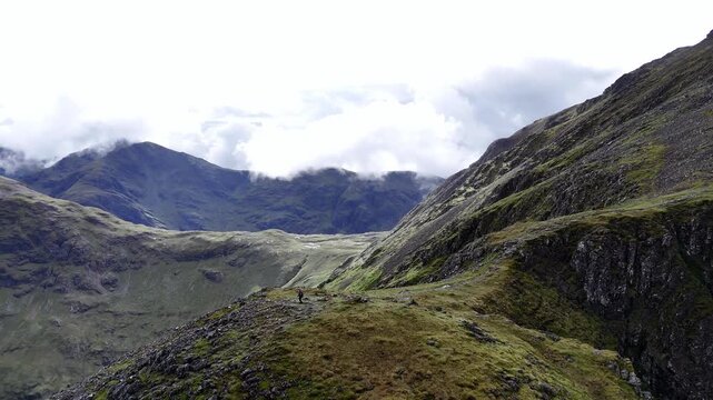 Aerial drone tracking shot captures a lone hiker on a rugged ridge near Stob Coire Sgreamhach part of Bidean nam Bian and the Three Sisters in the scottish Highlands, UK. The atmosphere feels serene.