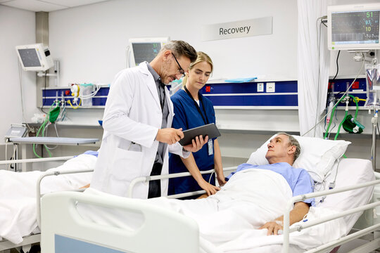 Doctor Checks Tablet While Patient Rests in Hospital