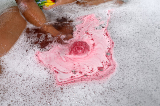 Pink effervescent bath bomb dissolving in a foaming bathtub close-up.