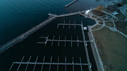 Fototapeten Pier A beautiful high-angle drone photograph looking down at rows of empty wooden boat docks in a calm harbor basin next to a paved park promenade and stone breakwater at early morning sunrise.  © Matt