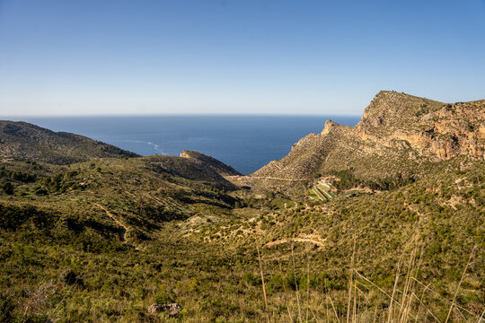 View of rugged hills and a deep valley leading towards the blue Mediterranean Sea under a clear sky Andratx, Balearic Islands, Spain.