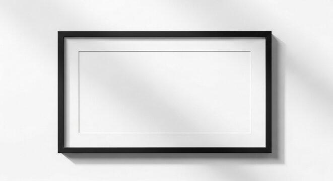 Elegant rectangular black wooden picture frame with a clean white mat board centered on a bright wall featuring soft natural shadows cast across the smooth surface for professional display purposes.