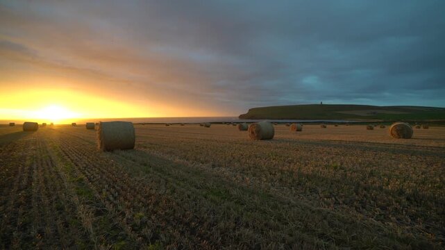 sunset over a field of straw bails looking over to kitchener's memorial in orkney