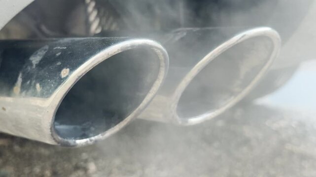 The dual chrome exhaust tips of a vehicle are expelling a thin cloud of white water vapor. The process produces a soft, low-frequency rumbling hiss or a steady, muffled "whoosh" sound.