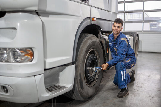 A smiling mechanic expertly uses a professional tool to unscrew a wheel from a truck in a well-lit workshop. The image captures his concentration and skill, showcasing automotive care.