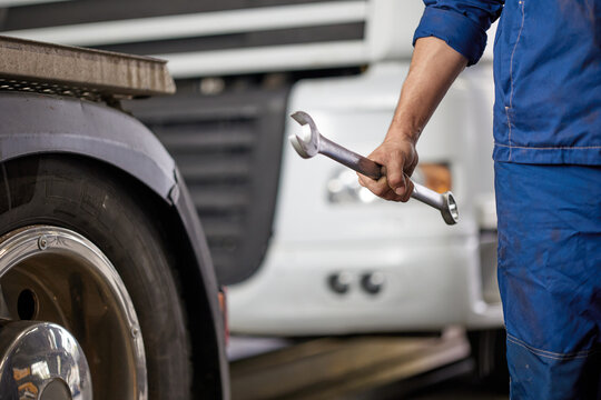 A skilled mechanic wearing blue overalls holds a wrench, standing confidently in front of a truck. This image symbolizes quality workmanship and dedication to automotive care.