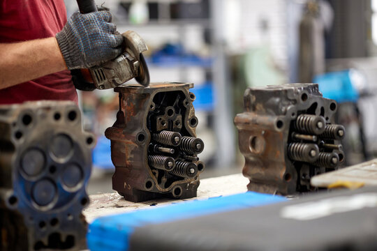 A skilled mechanic is meticulously cleaning a truck cylinder head using a grinder in a well-equipped maintenance shop. The scene showcases the professionalism and expertise in automotive repair.