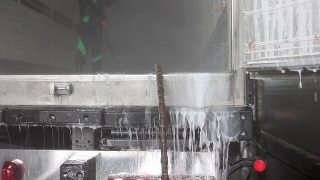 A dedicated man in overalls meticulously cleans the interior of a heavy truck semi-trailer, showcasing his professionalism and attention to detail in maintaining vehicle cleanliness.