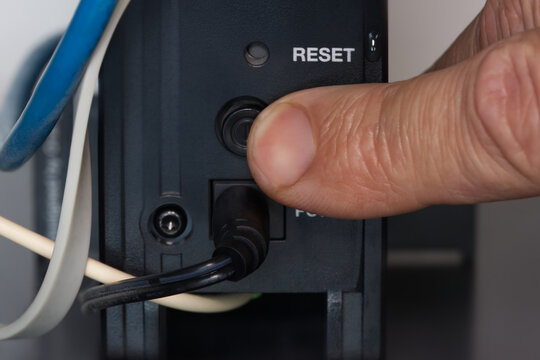 Finger pressing the reset button on the back of the internet router to resolve the home Wi-Fi network issue.