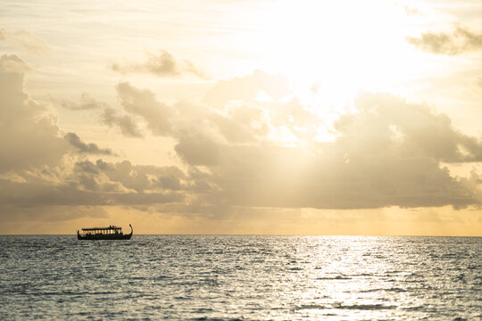 View of a traditional dhoni boat sailing on the calm Indian Ocean under a golden sunset sky with soft clouds Dhigurah, Alif Dhaal Atoll, Maldives.