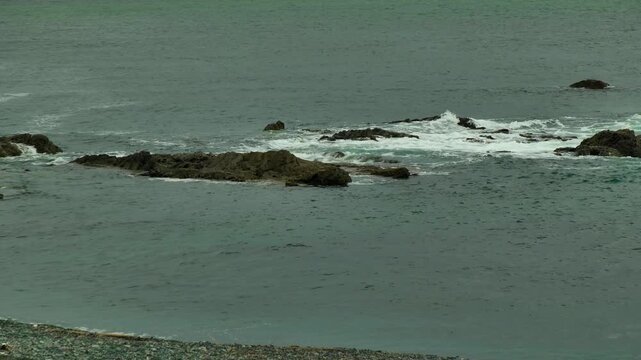 曇天の荒々しい海と岩場に打ち付ける白い波の風景
