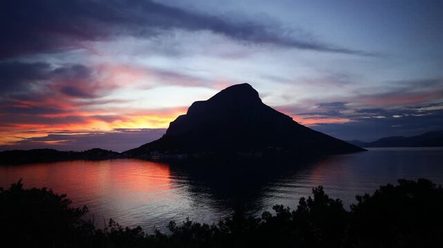Breathtaking sunset over Telendos, a picturesque island in the Aegean Sea near Kalymnos. Warm golden and orange light bathes the rugged limestone cliffs, tranquil sea, and traditional waterfront