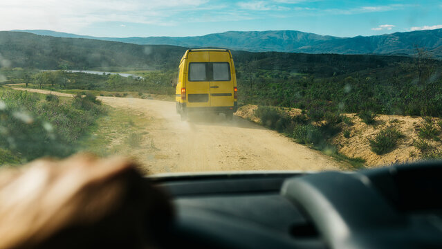 Camper van driving on dusty road through mountain valley