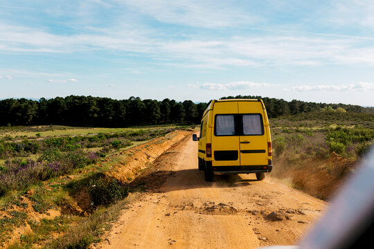Yellow camper van driving on dusty road in countryside
