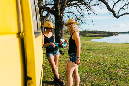 Two women with ukulele by camper on lakeside holiday