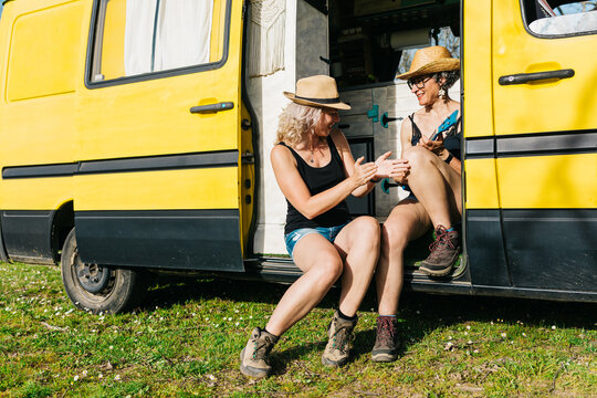 Two women with ukulele relaxing by yellow camper van