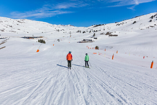 Couple skiing down snowy mountain slope under blue sky