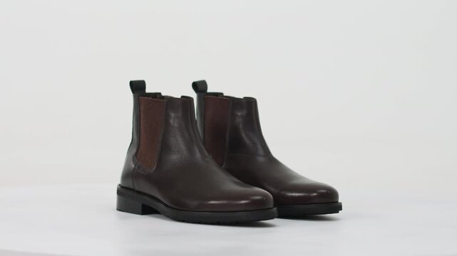 Brown leather men's Chelsea boots rotating on a turntable isolated on a white background for e-commerce
