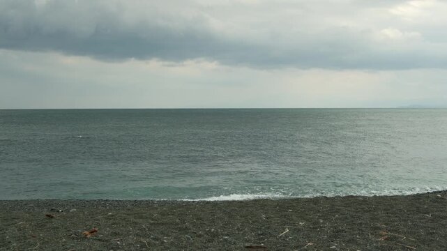 穏やかな曇天の海と水平線に広がる厚い雲が創り出す静寂の海岸線