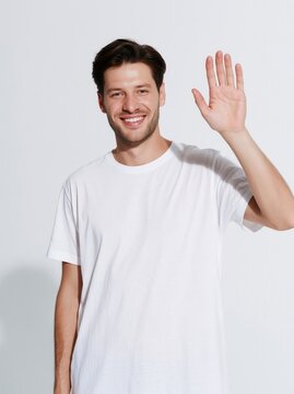 Young smiling man waves his hand to say hello.	