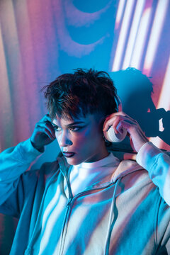 Young woman in hoodie listening to headphones in neon light