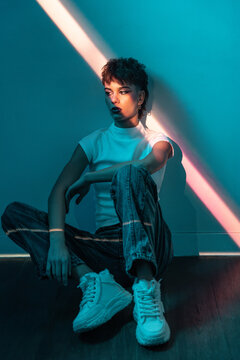 Young woman in neon light sitting indoors, moody portrait