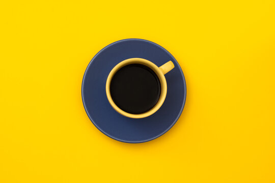 Black coffee in yellow cup on blue saucer, top view