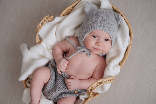 One-month-old baby boy in knit bonnet resting in basket