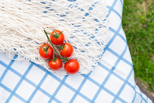 Fresh cherry tomatoes in net bag on picnic cloth outdoors