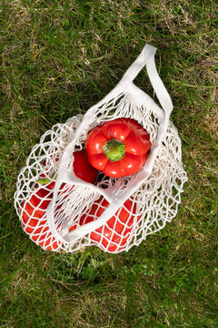 Reusable mesh bag with red bell peppers on green grass