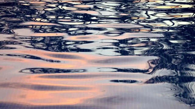 A static 4K video shot capturing the gentle ripples of a swimming pool at sunrise, featuring abstract reflections of warm golden morning light
