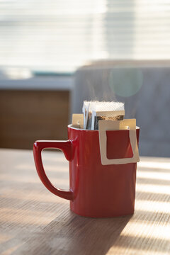 Steaming coffee in red mug with filter on sunny table