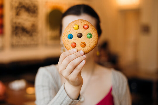 Woman holding candy cookie in cozy cafe, face hidden