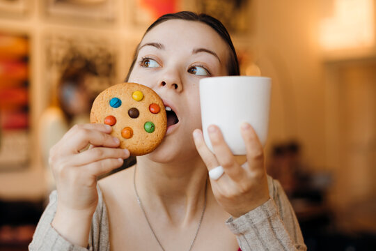 Woman enjoying coffee and colorful cookie in cozy cafe
