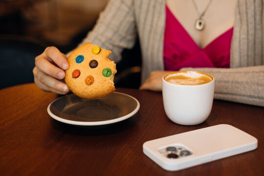 Woman enjoying cookie and latte at cafe table with phone