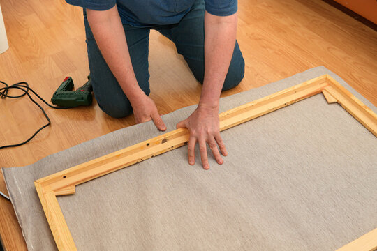 Person stretching canvas on wooden stretcher frame at home