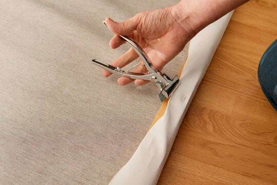 Hand using tension clamp to stretch canvas on wooden frame