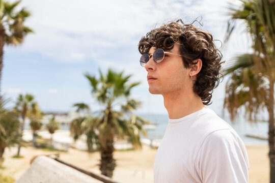 Curly haired man in sunglasses enjoying seaside lifestyle