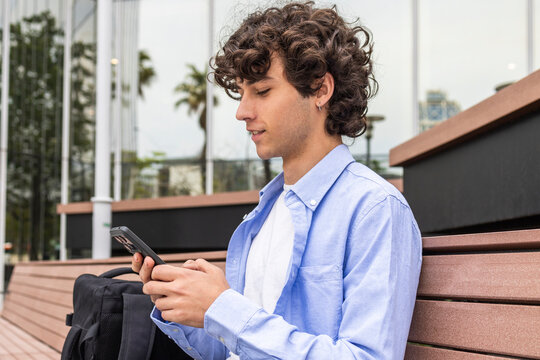 Curly-haired man using smartphone on city bench outdoors