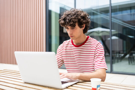 Curly-haired man working on laptop at outdoor cafe table