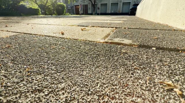 Bright morning light glints off the rough stone paving tiles of a public walkway. The calm urban scene is surrounded by a continuous, low-frequency hum of distant city traffic.